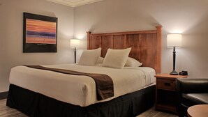 Un cuarto de hotel con una cama grande, dos mesitas de noche con lámparas, una silla y un cuadro enmarcado en la pared.
