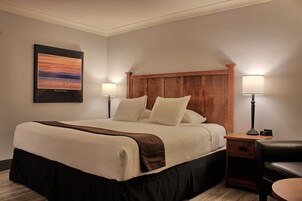 A hotel room with a large bed, two bedside tables with lamps, a chair, and a framed picture on the wall.