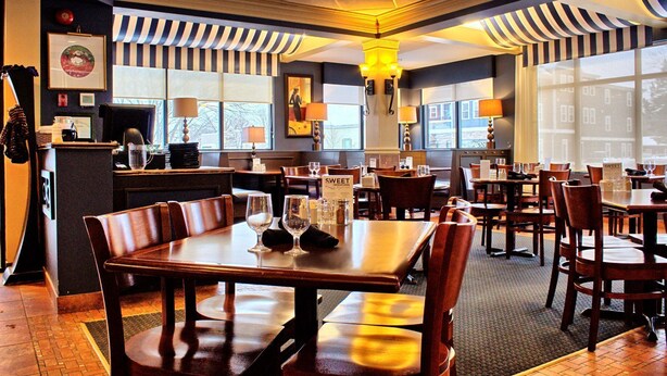 Un restaurante con mesas y sillas de madera, ventanas amplias y decoraciones con rayas en el techo.
