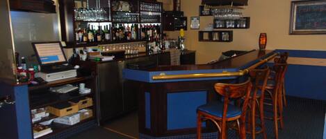 A bar area with a counter, stools, and shelves stocked with bottles and glasses.