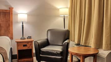 Una camera d'hotel con una poltrona in pelle, due abat-jour, un comodino in legno, un tavolino e una finestra con tende color beige.