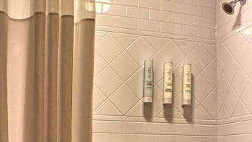 Een badkamer met een bad, een douchekop en drie toiletartikelen op de muur.