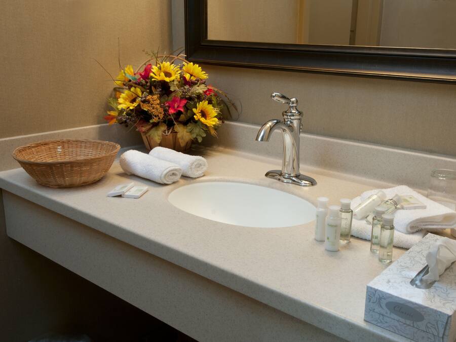 A bathroom sink with a mirror, a basket, towels, and toiletries.