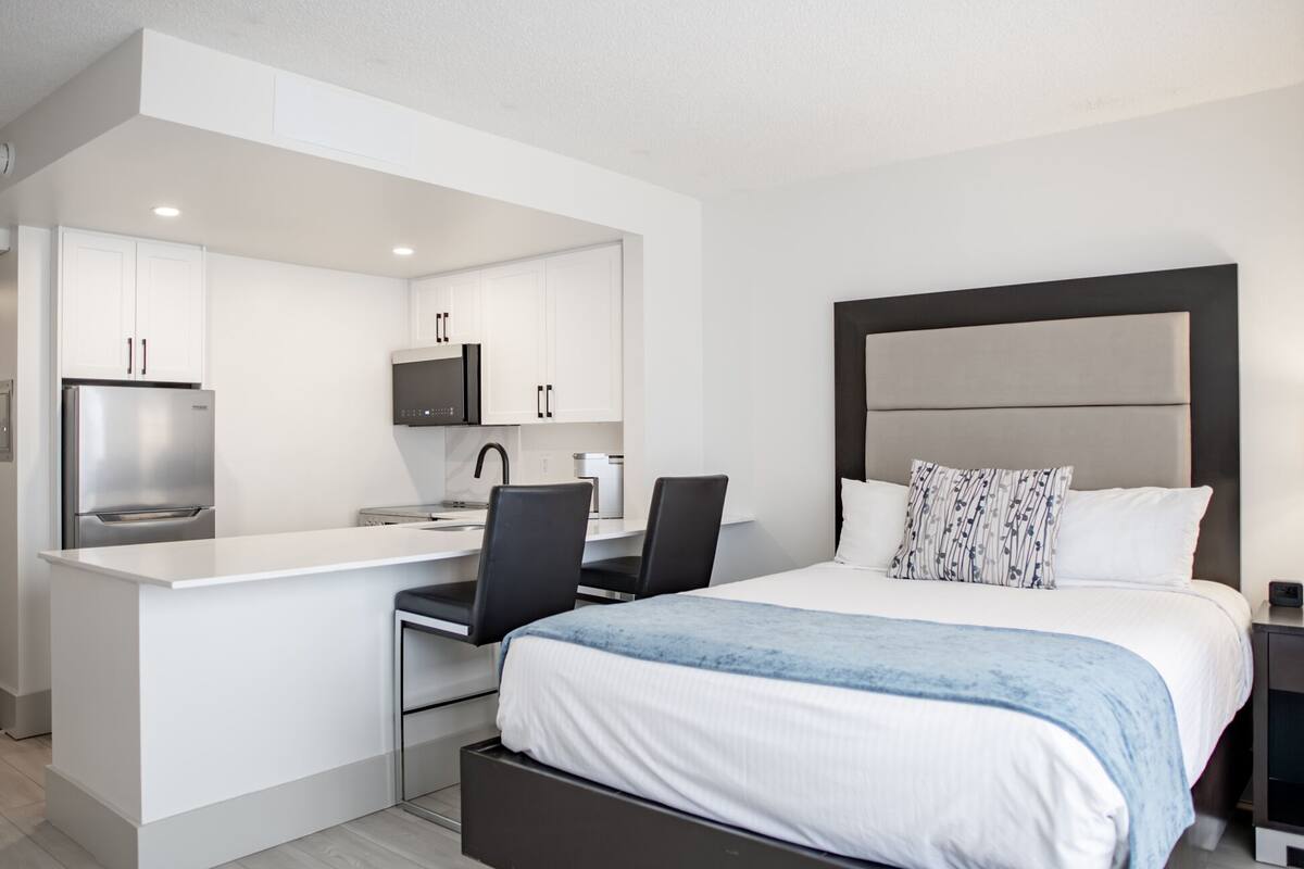 A modern hotel room with a bed, a desk with a chair, a microwave, and a refrigerator.