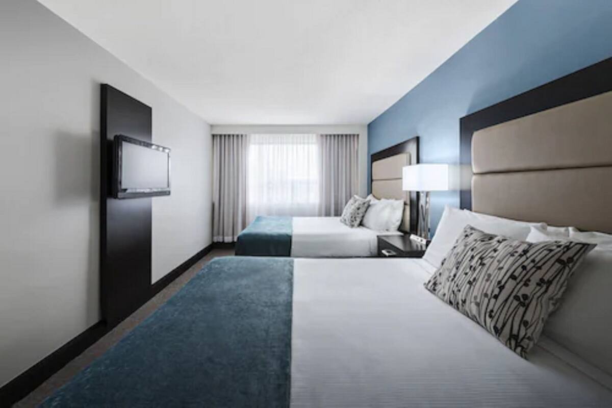 A hotel room with a large bed, a smaller bed, a TV mounted on the wall, and a window with curtains.