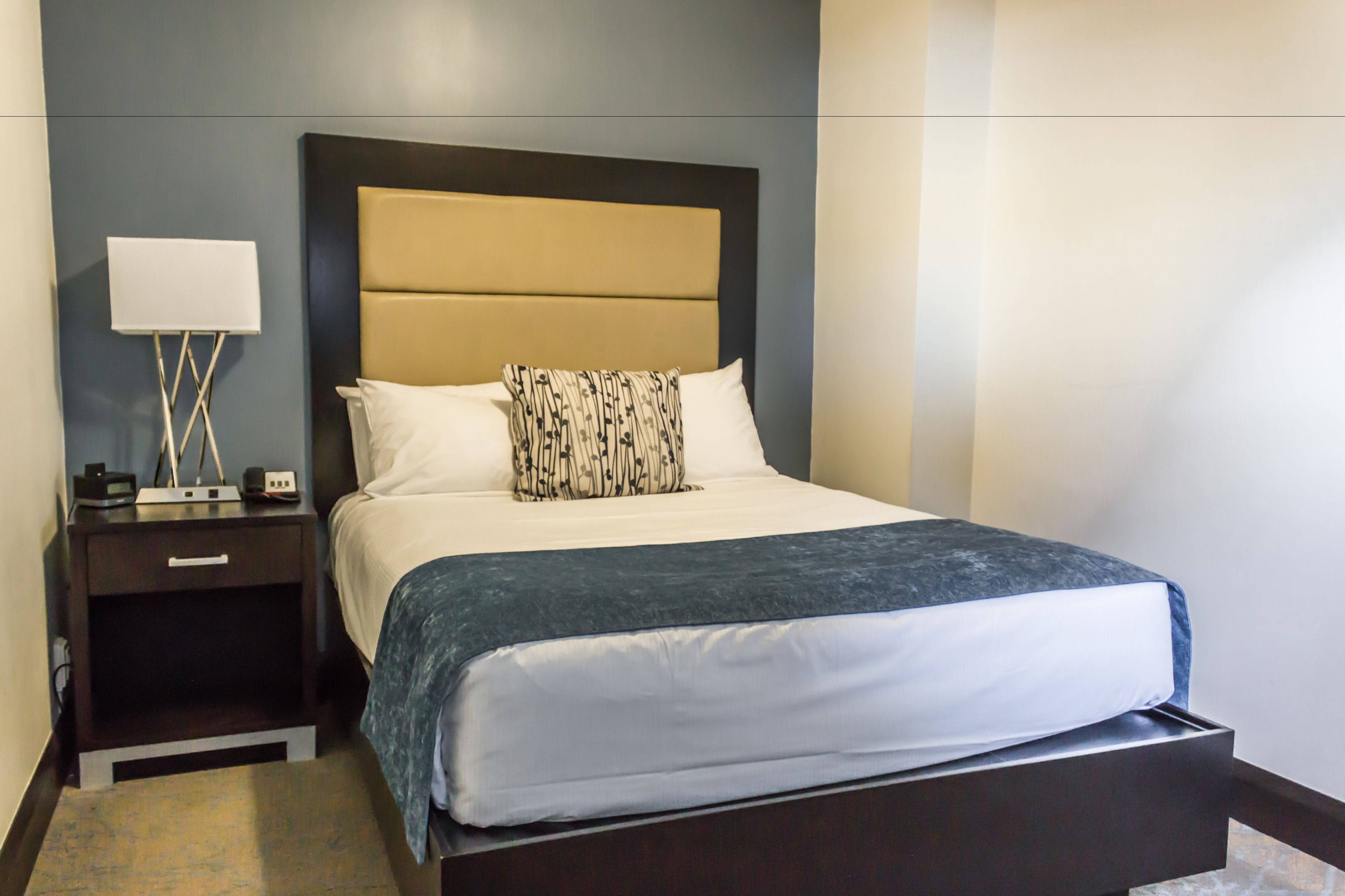 A neatly made bed with a patterned pillow, a bedside table with a lamp, and a modern headboard.