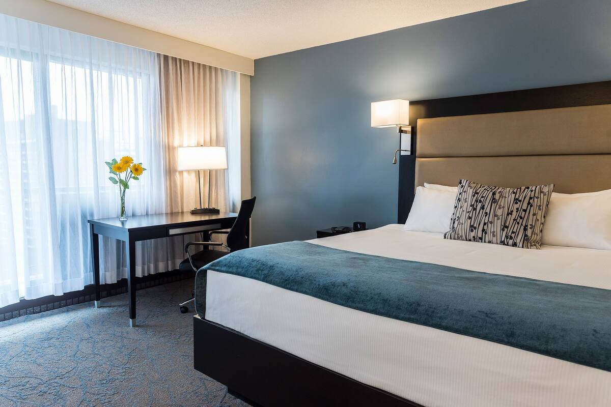 A hotel room with a large bed, a desk with a lamp, and a chair.