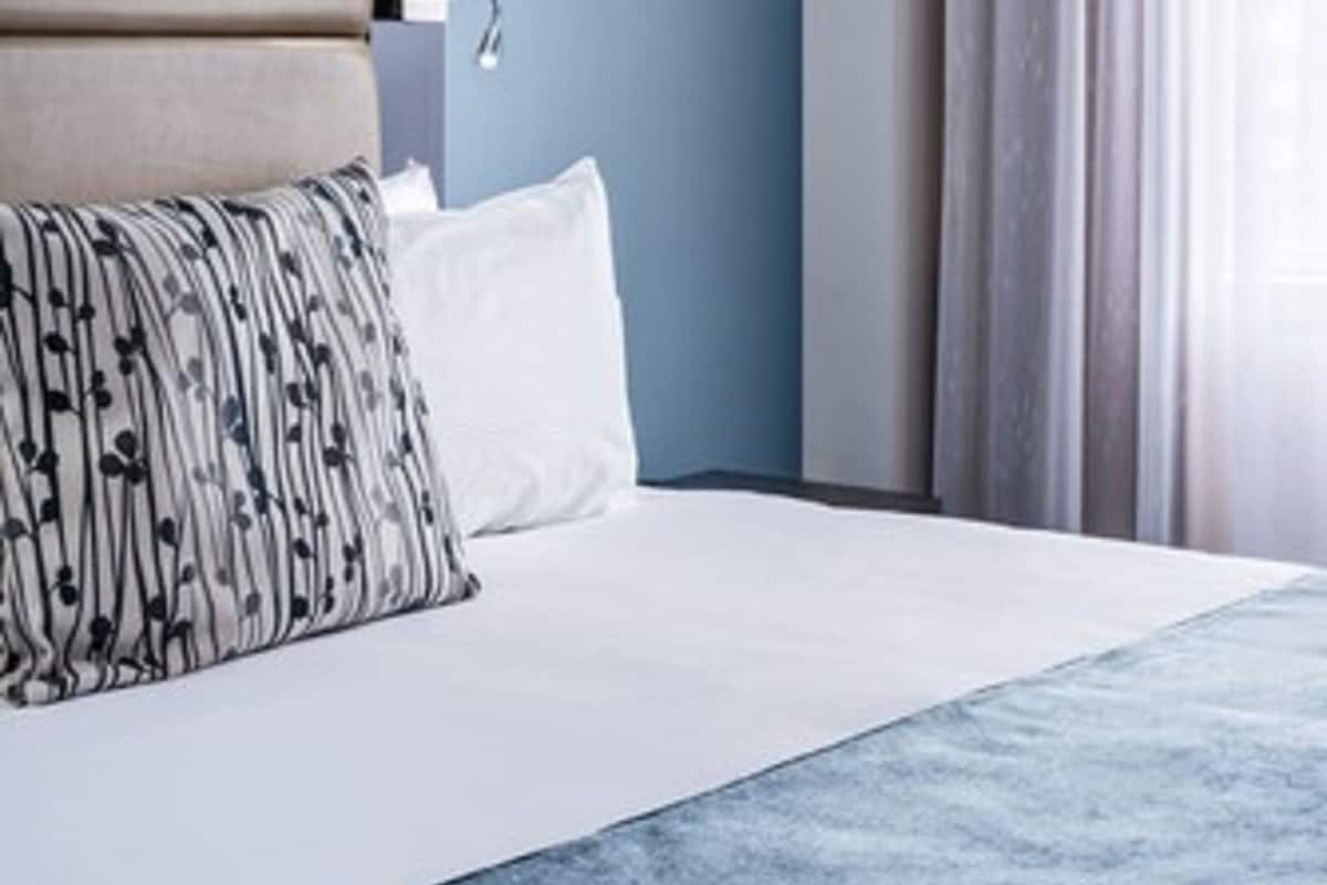 A hotel room with a bed, a headboard, a bedside table, a lamp, and a window with curtains.