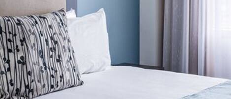 Een hotelkamer met een bed, hoofdeinde, nachtkastje, lamp en een raam met gordijnen.