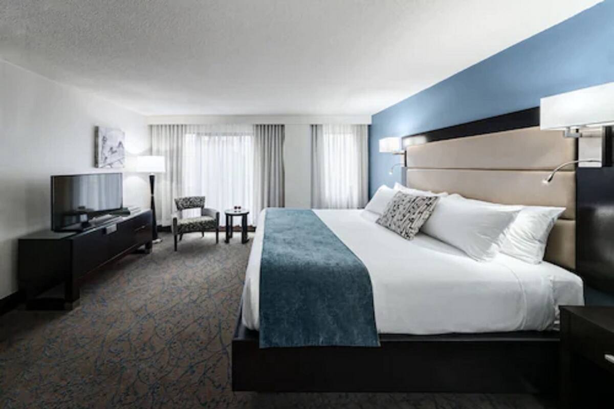 A hotel room with a large bed, a television, a desk, and a chair.