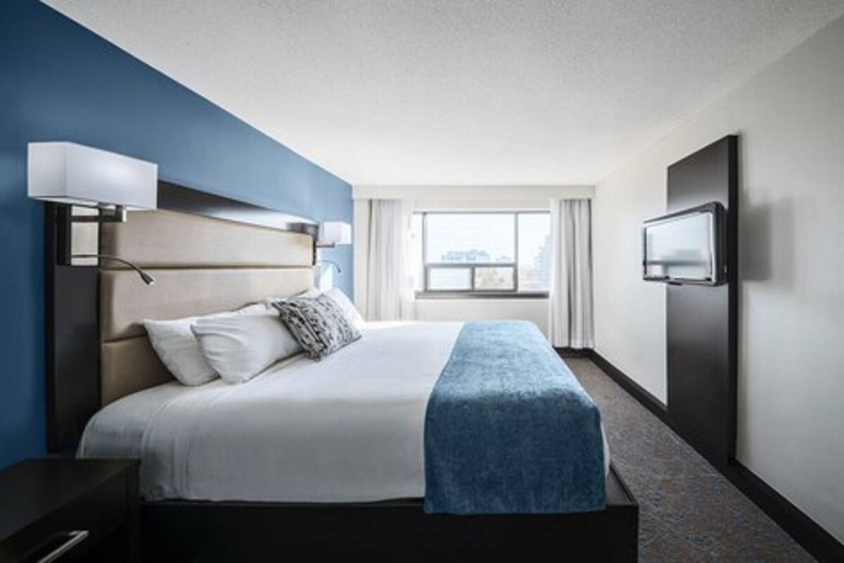 A hotel room with a bed, a TV, a nightstand, and a window with curtains.