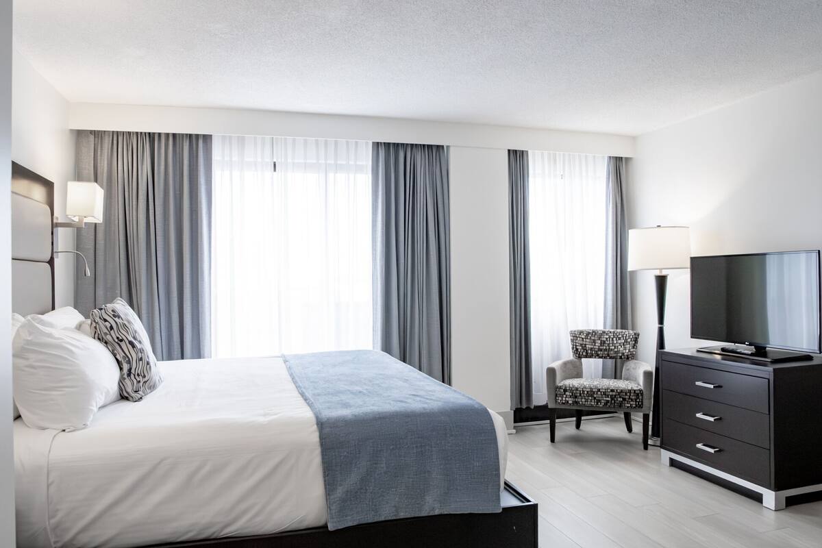 A modern hotel room with a bed, a TV, a desk, and a chair.