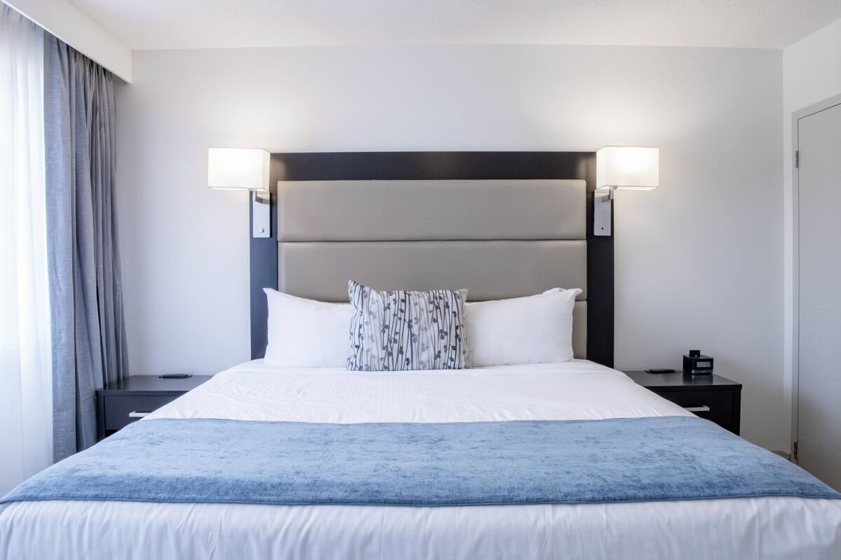 A hotel room with a large bed, two bedside tables, a nightstand, a lamp, and a window with curtains.