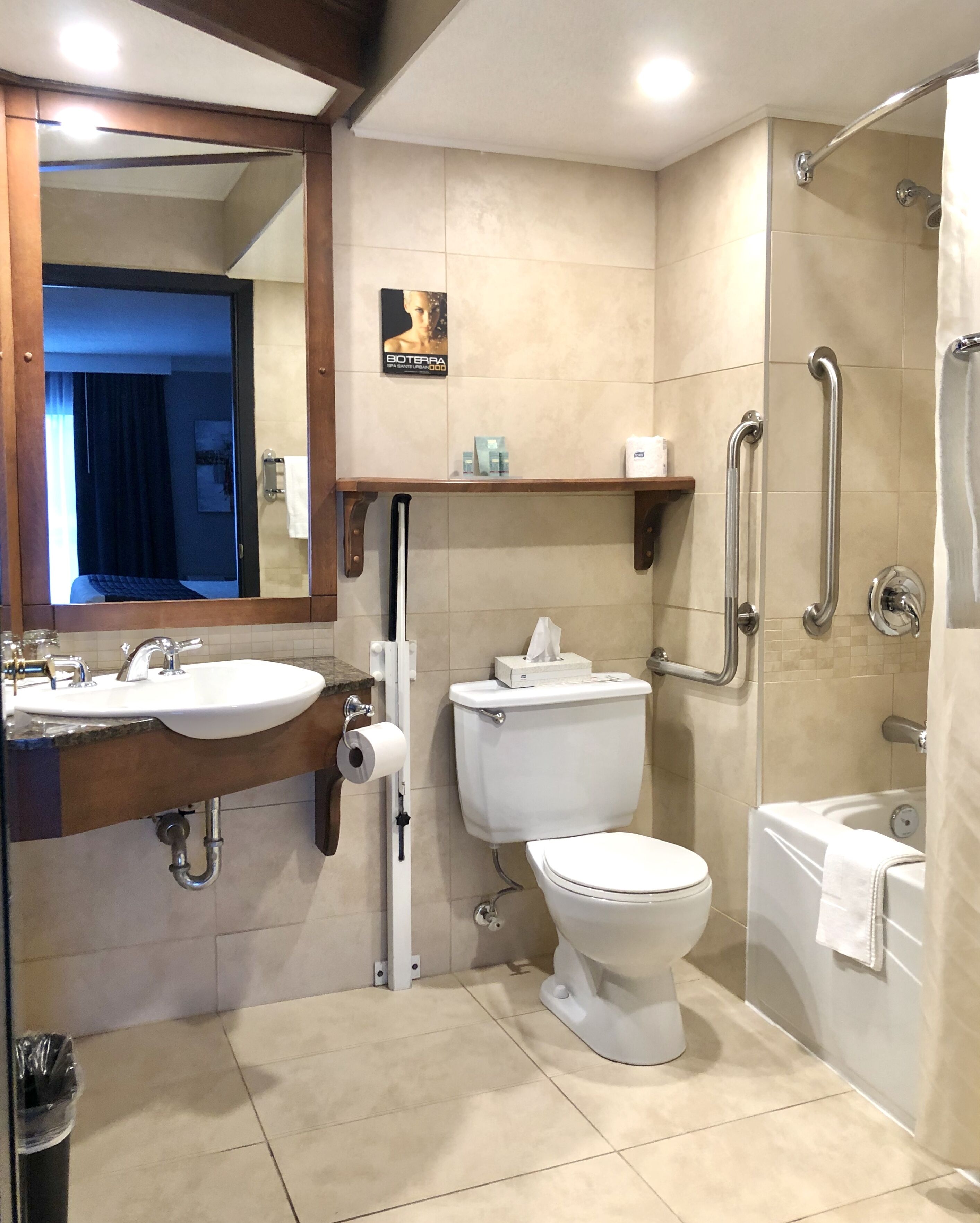 A modern bathroom with a sink, toilet, and shower. It includes a mirror, towel rack, and a toilet paper holder.