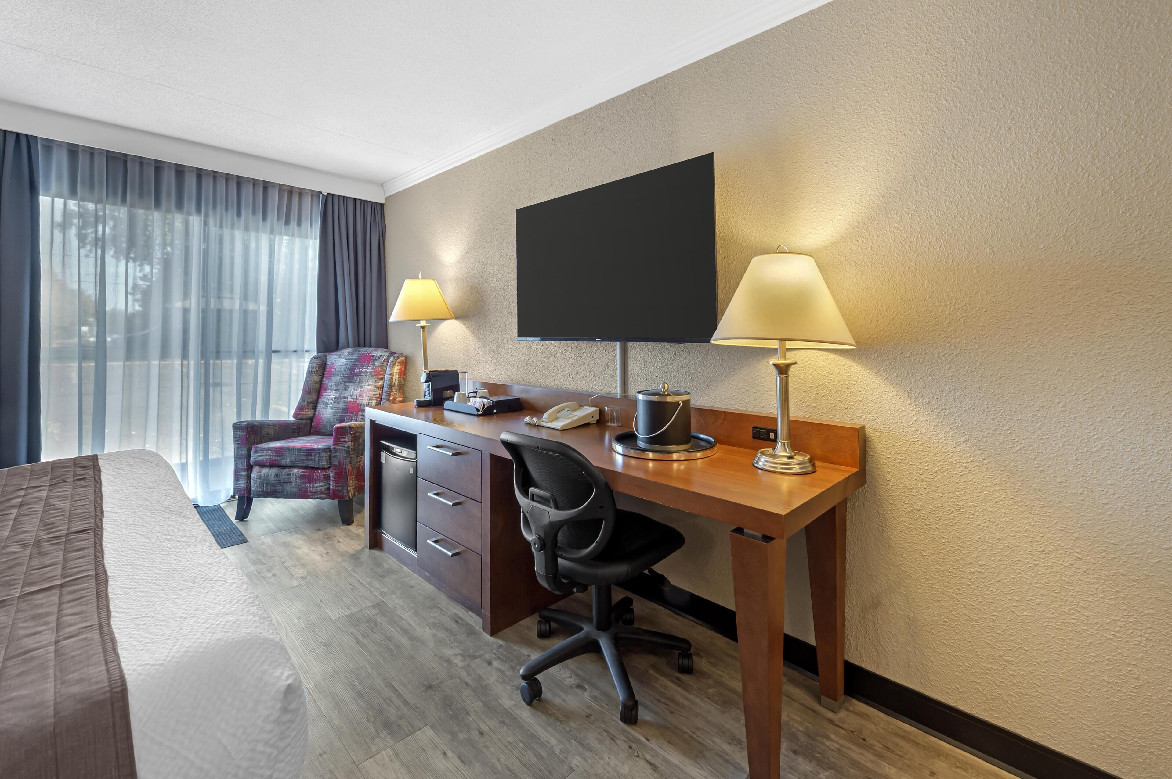 Habitación de hotel con cama, escritorio con computadora, silla, televisor y dos lámparas.