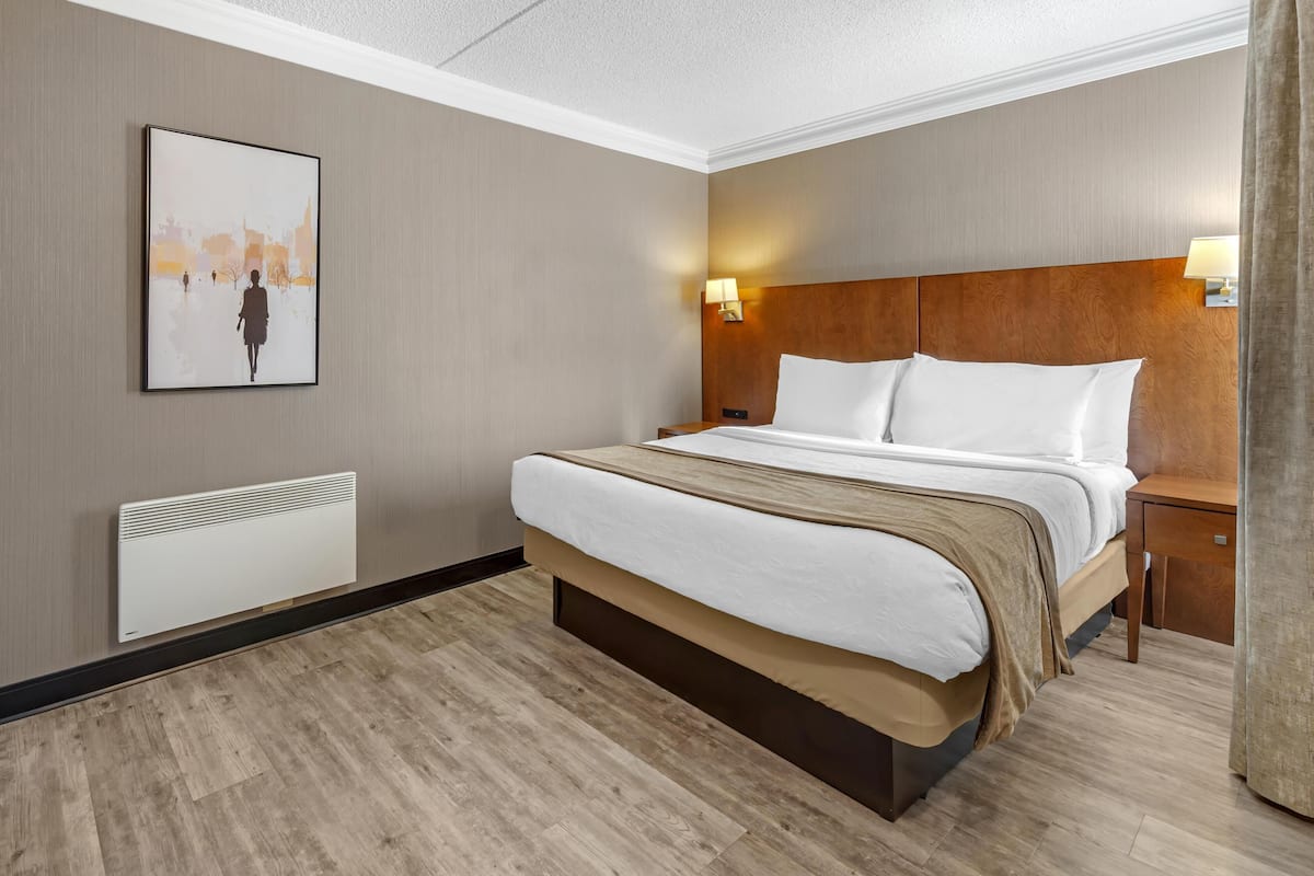 Habitación de hotel con una cama grande, cabecero, mesita de noche, lámpara y radiador fijado a la pared.