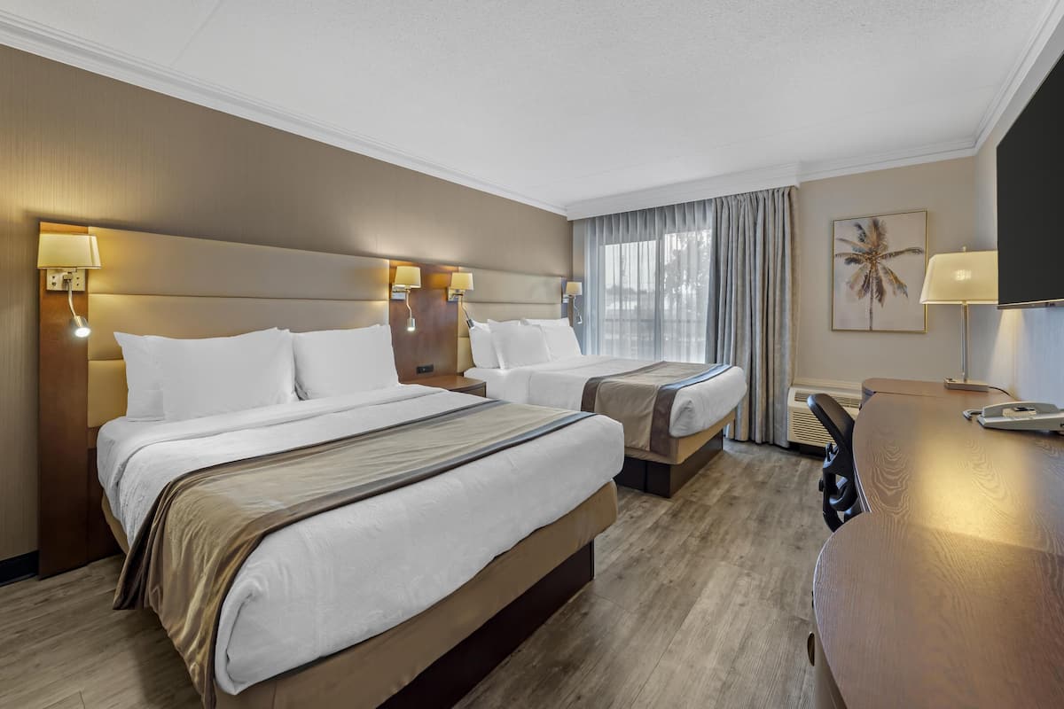 Una habitación de hotel con dos camas, un escritorio y un ventanal con cortinas.