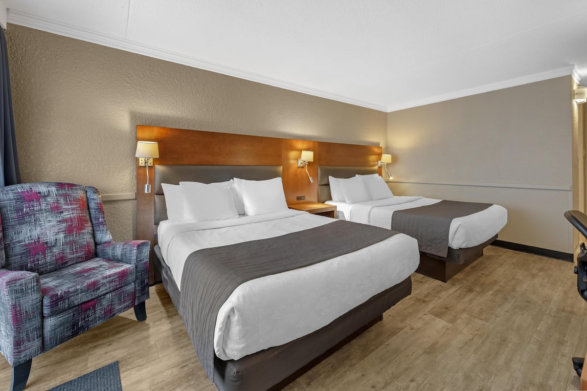 Habitación de hotel con dos camas, una silla y un escritorio.