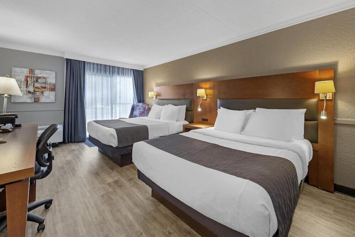 Habitación de hotel con dos camas, un escritorio, una silla y una ventana con cortinas.
