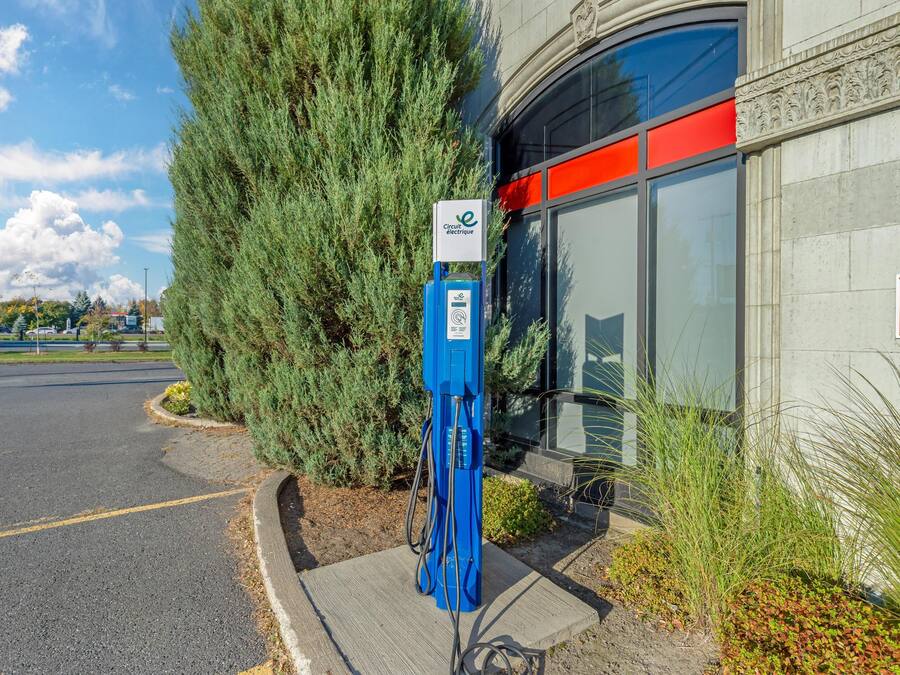 A blue electric vehicle charging station in front of a building with a red and white sign that reads "ZONE AGRAR BEST".