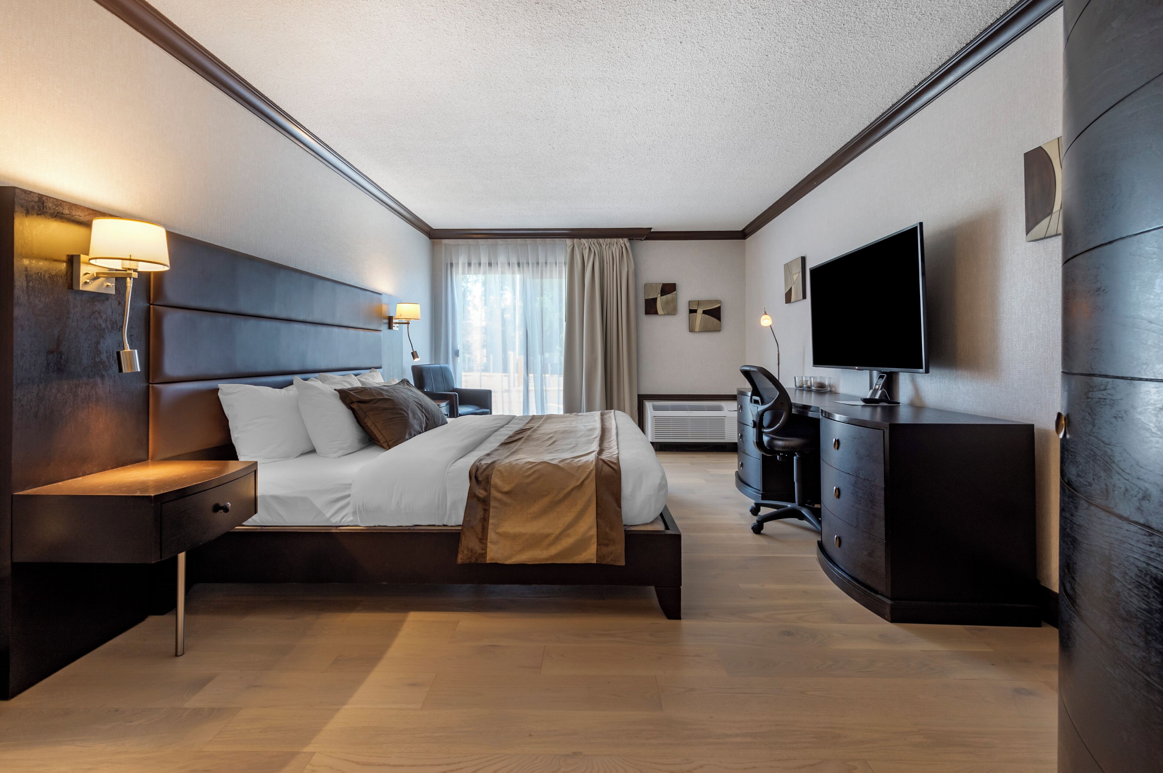 A modern hotel room with a large bed, bedside lamps, a flat-screen TV, a desk, and a wardrobe.
