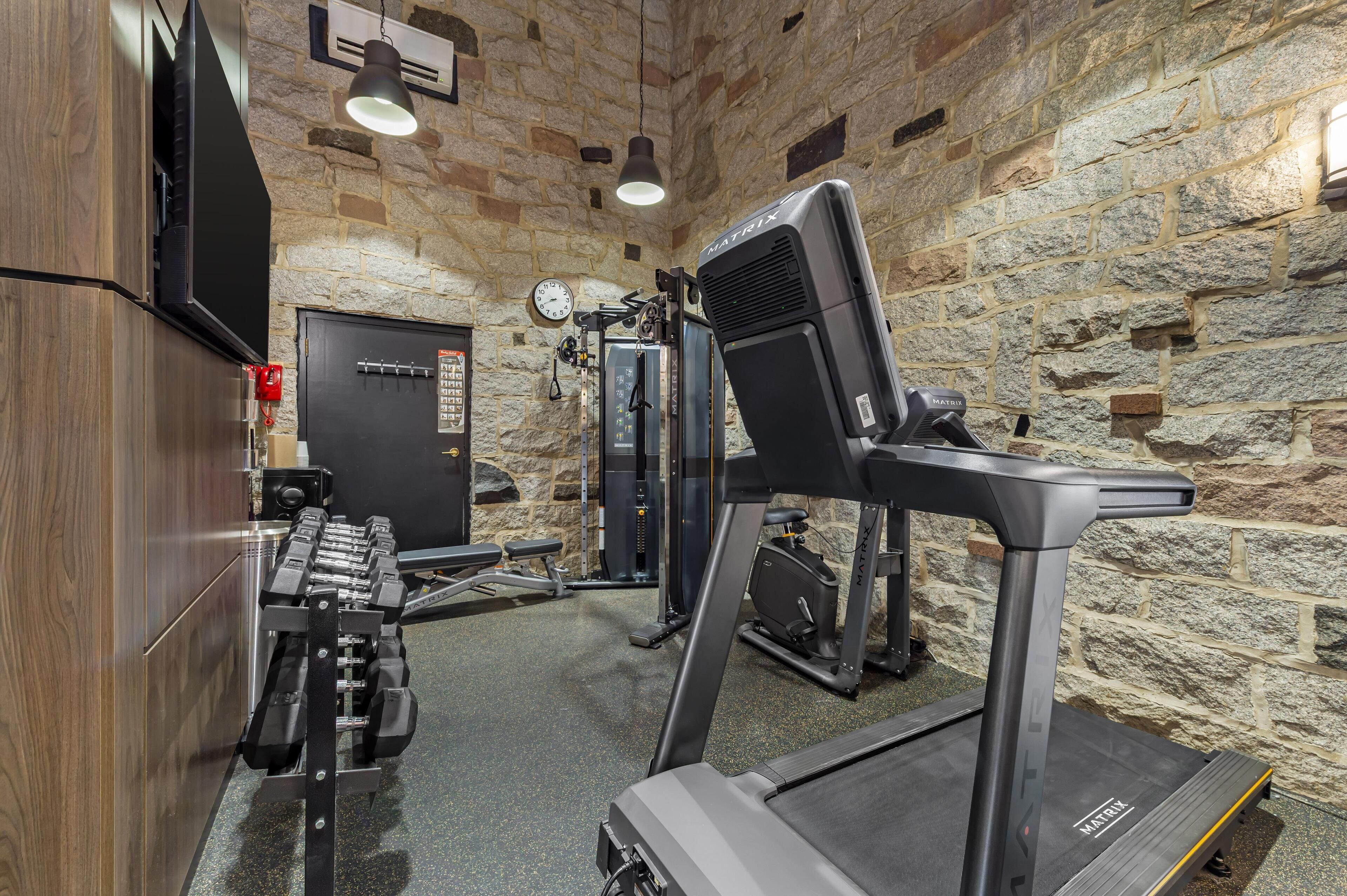 A gym with a treadmill, weight machines, and a wall clock.