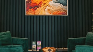 Una habitación con dos sillones verdes, una mesa de centro redonda con un adorno de madera, y un cuadro abstracto grande en la pared.