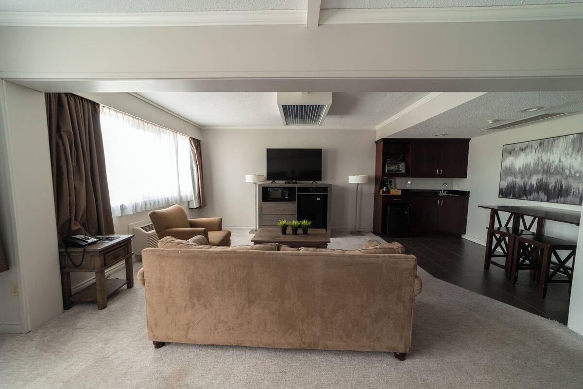 Una sala de estar con un sofá color beige, un televisor de pantalla plana y una zona de comedor con una mesa y sillas.