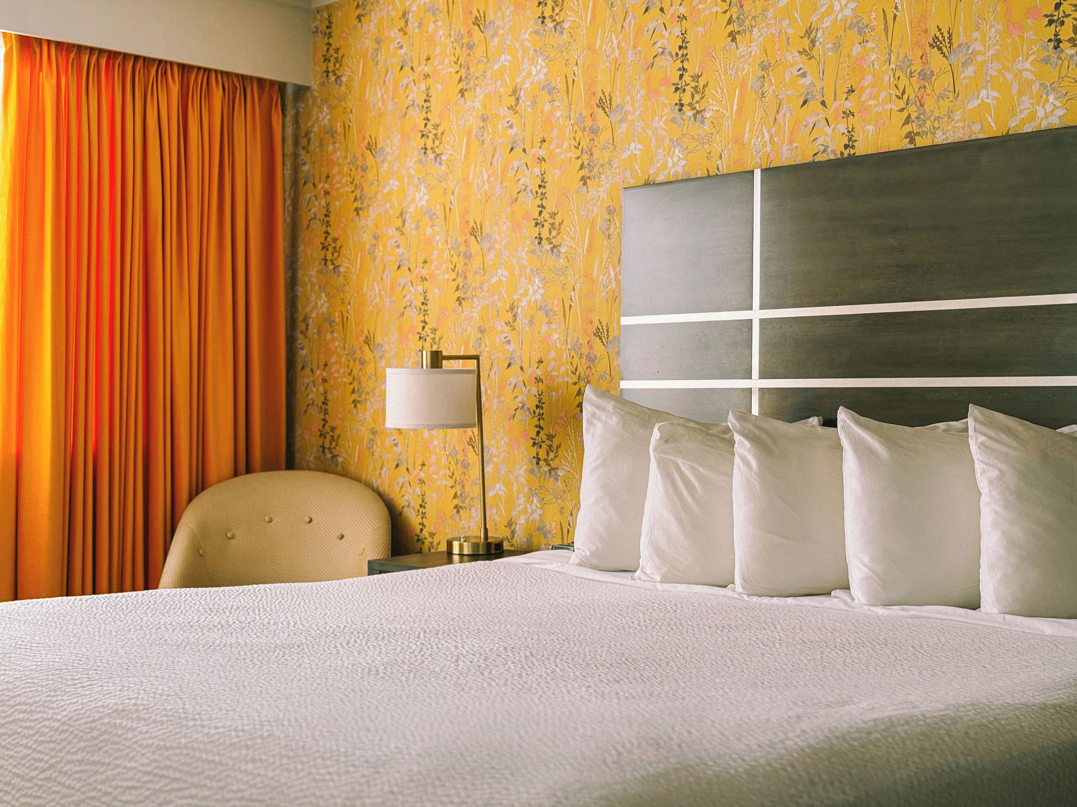 Ein Hotelzimmer mit Bett, Stuhl, Nachttisch, Lampe und blumigem Wandpapier.