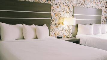 A hotel room with two beds, a nightstand with a lamp, and floral wallpaper.