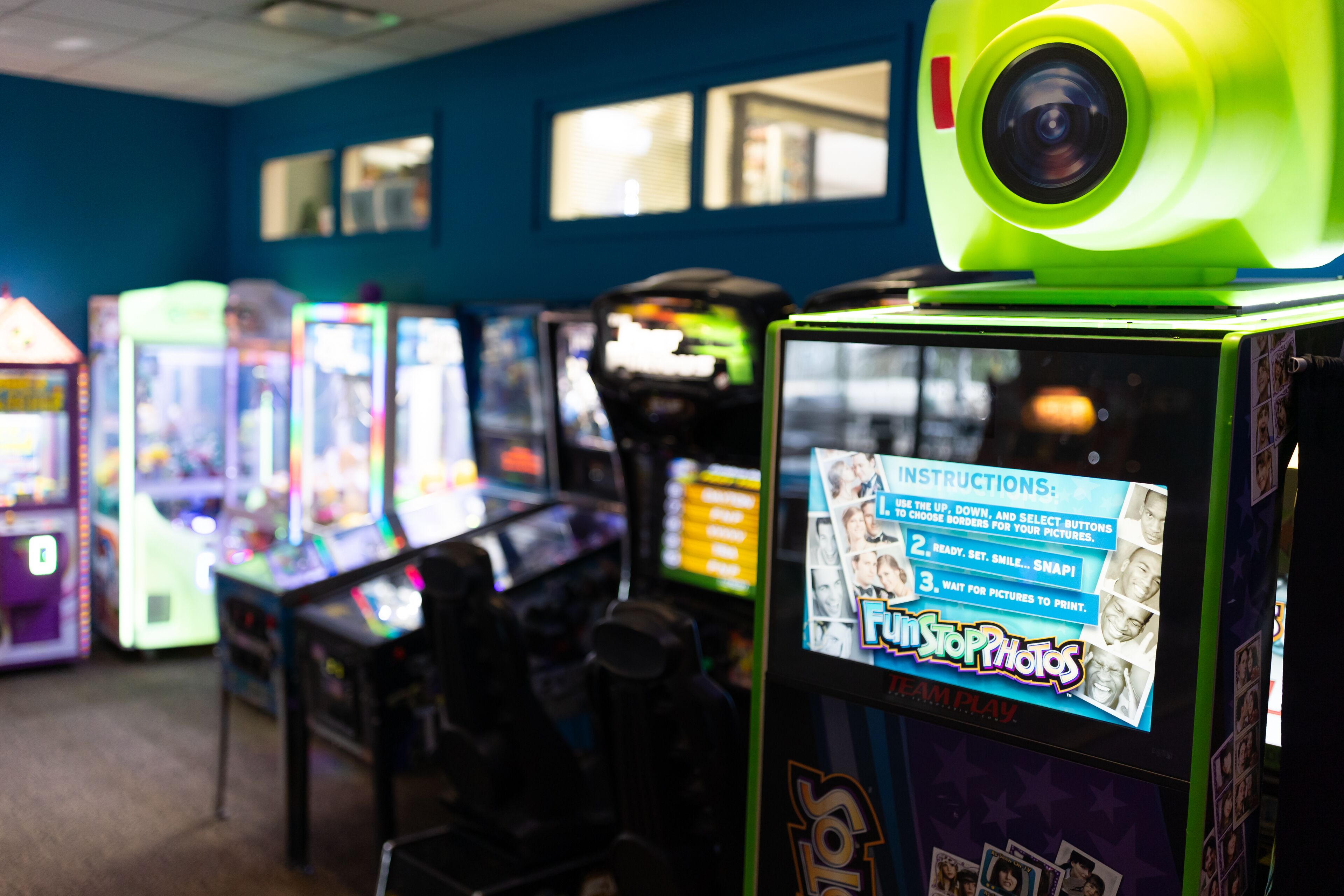 A row of arcade machines with a neon green top, including a 'FunStopPhotos' machine with instructions on the screen.
