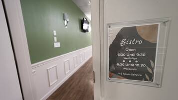 A hallway with a green wall and a sign indicating the Bistro's operating hours.