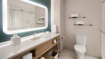 A modern bathroom with a large mirror, white sink, and toilet. There are shelves with towels and toiletries.