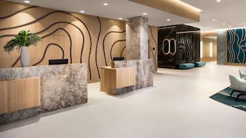 A modern reception area with marble counters, wooden panels, and a seating area with blue upholstered chairs.