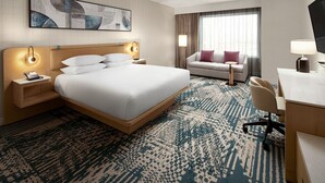 A hotel room with a large bed, a desk, a chair, a sofa, and a TV.