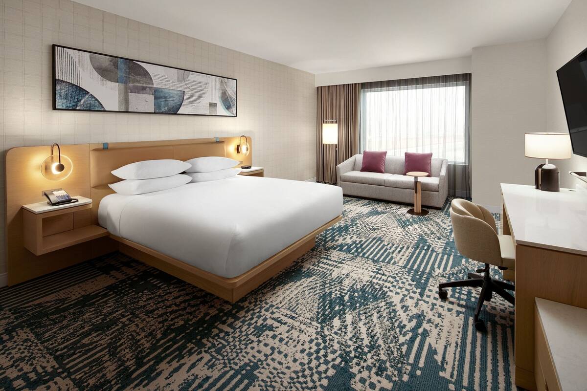 Quarto de hotel com uma cama grande, uma escrivaninha, uma cadeira, um sofá e uma televisão.