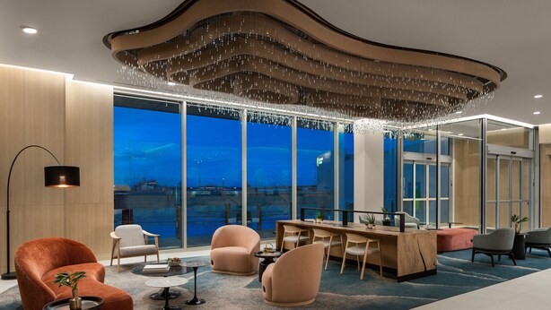 A modern interior with a curved ceiling, a large window overlooking a body of water, and a seating area with a wooden desk and chairs.