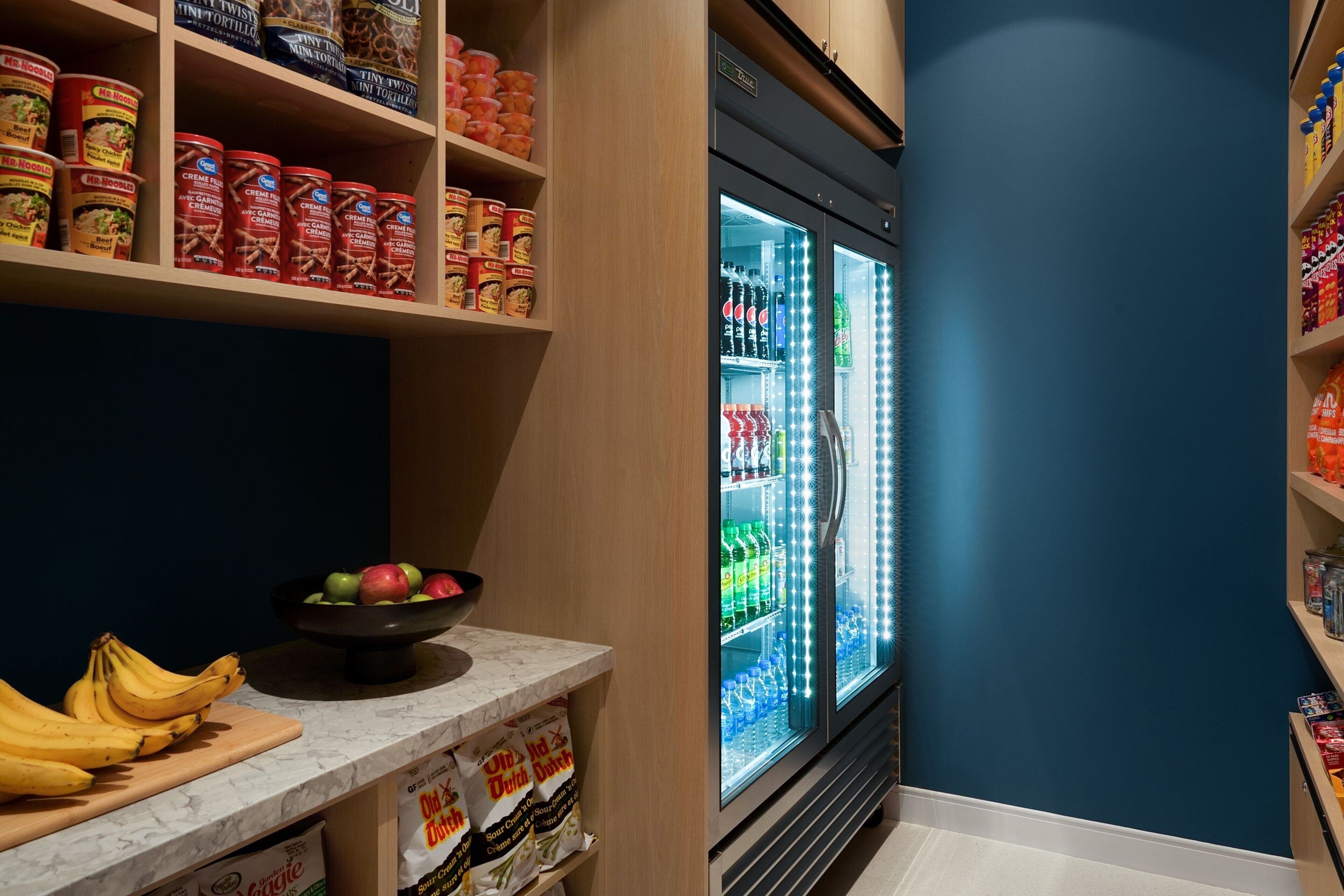 A kitchen area with a marble countertop, a bowl of fruit, and a refrigerator stocked with beverages.