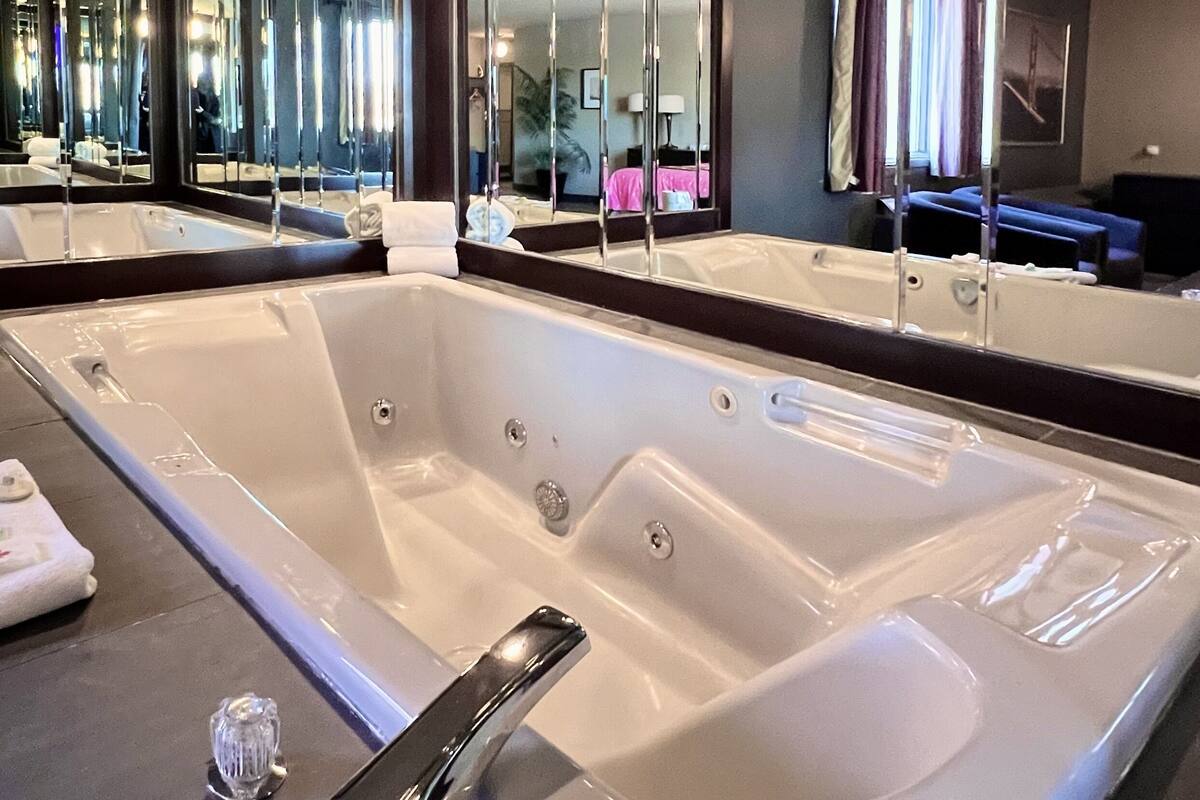 A modern bathroom with a large bathtub, a mirror, and a sink.