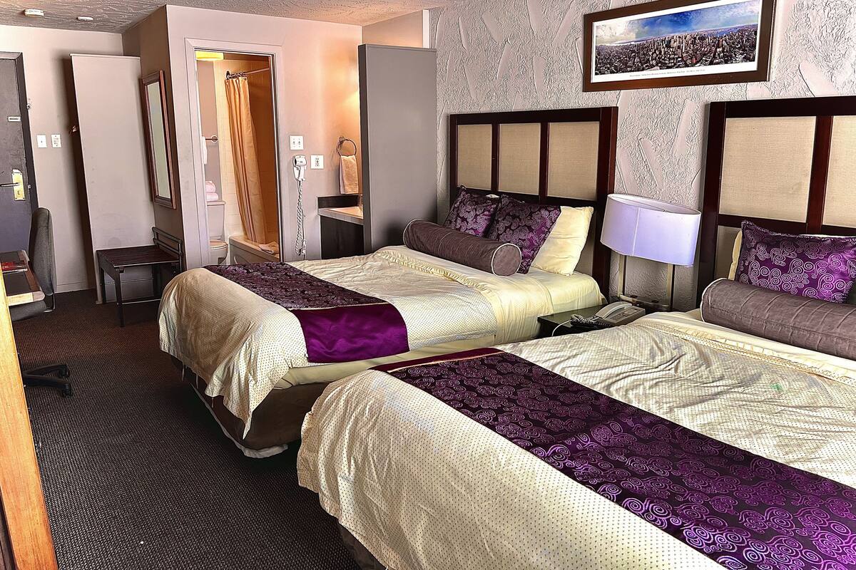 A hotel room with two beds, a desk, a chair, a bathroom, and a framed picture on the wall.