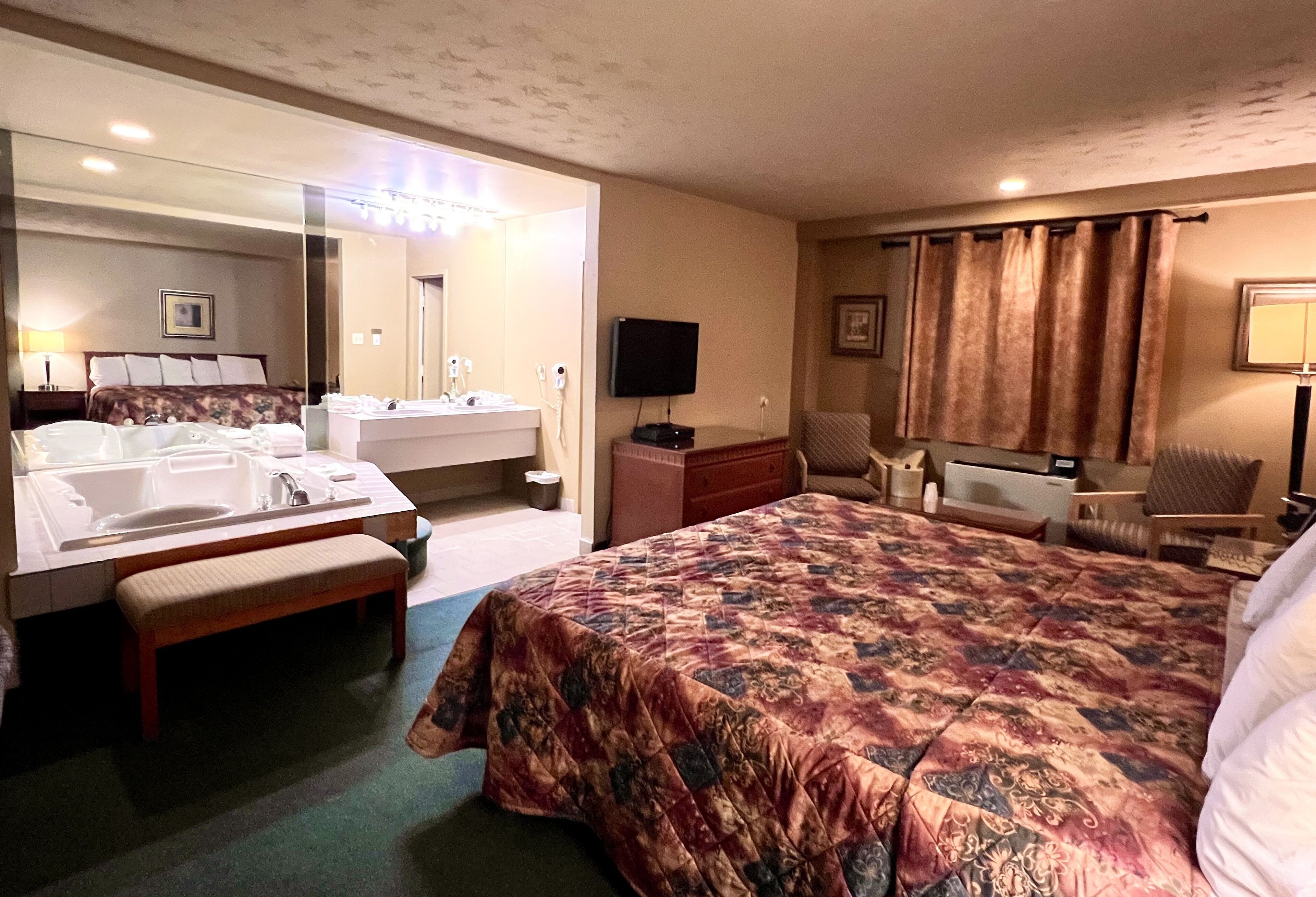 Une chambre d’hôtel avec un grand lit, une salle de bain avec un lavabo et un miroir, une télévision et un bureau avec une chaise.
