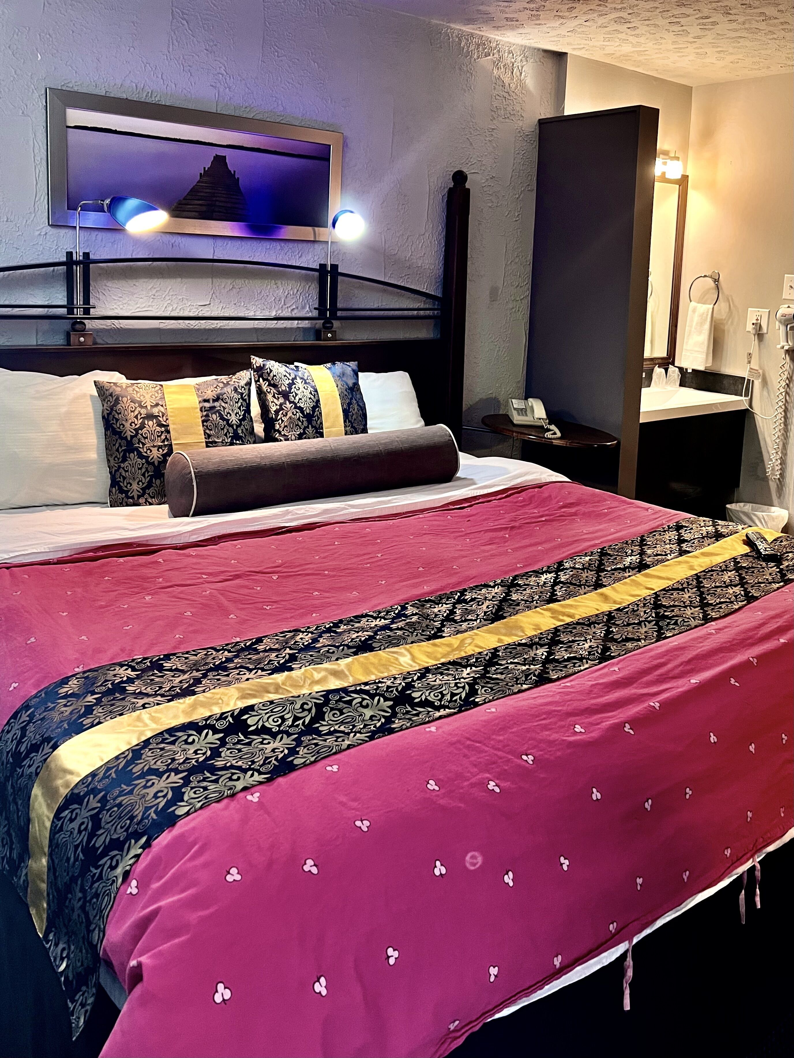 Ein Hotelzimmer mit einem großen Bett, einem Nachttisch, einem Spiegel und einem an der Wand befestigten Fernseher.