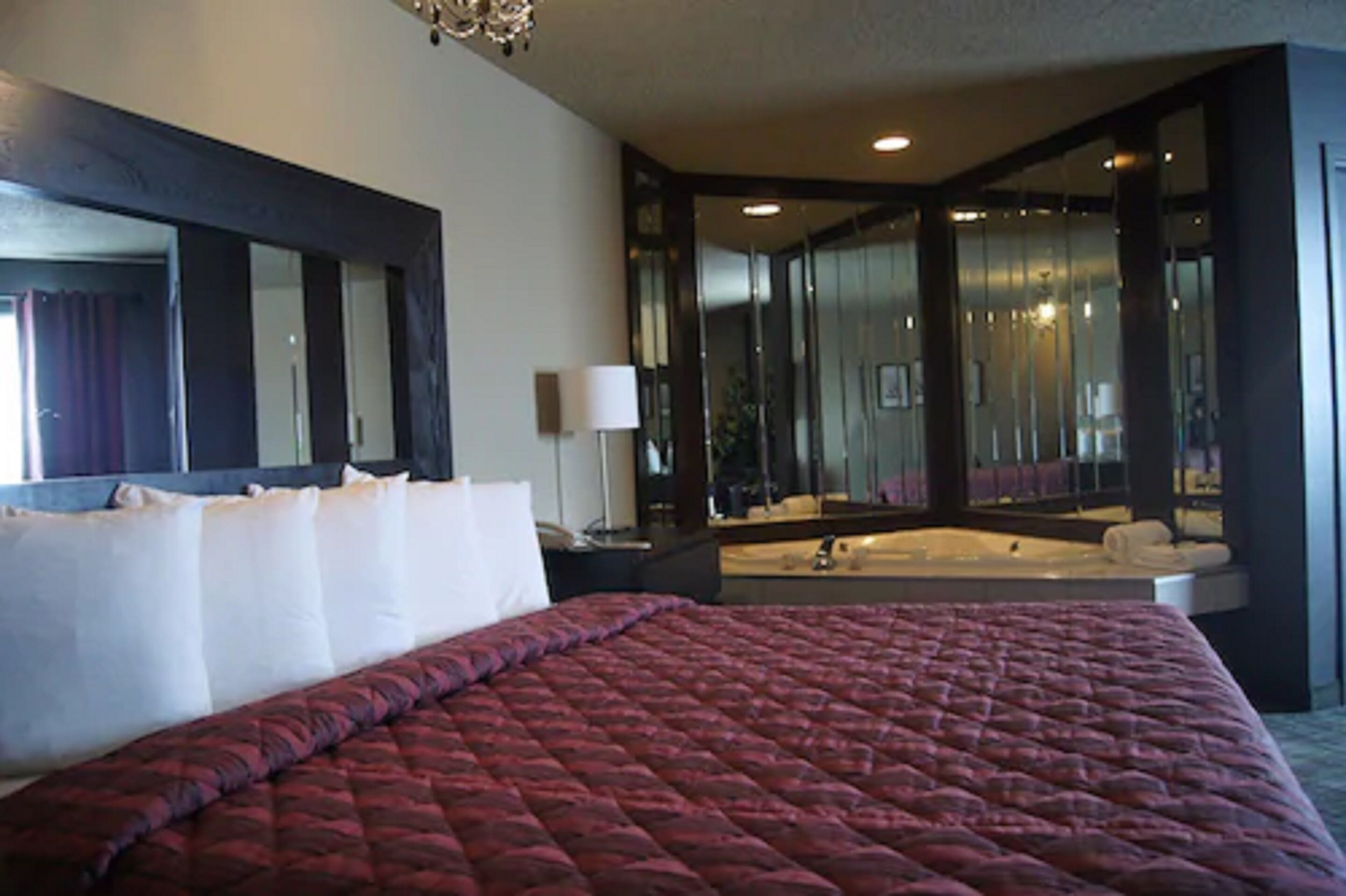 Quarto de hotel com uma cama grande, um espelho, uma mesa de cabeceira e um banheiro com banheira.