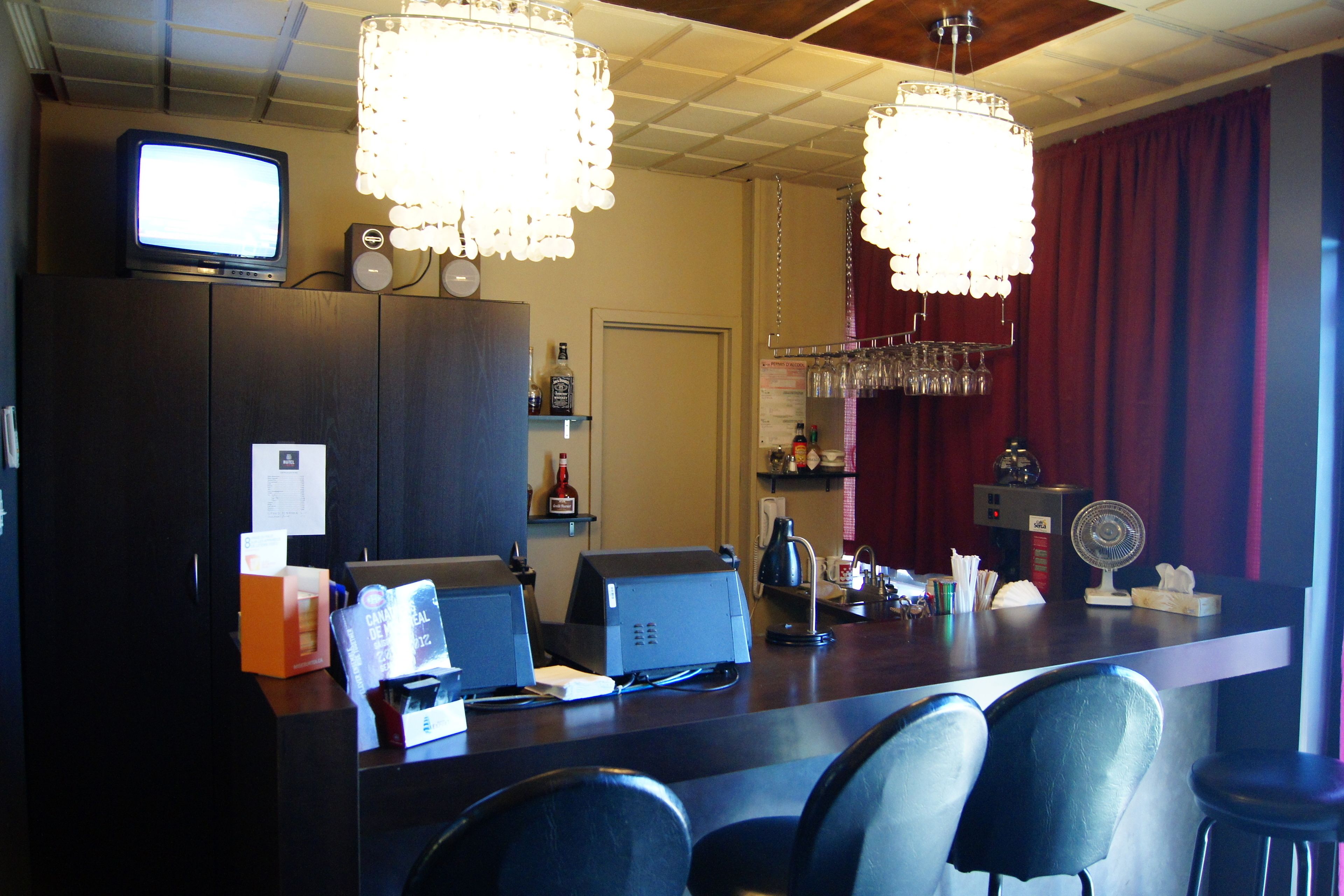 A bar area with a television, bar stools, a cash register, and a fan.