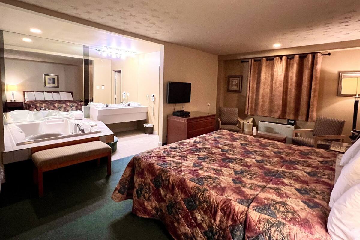 A hotel room with a large bed, a double sink, a television, a chair, and a desk.