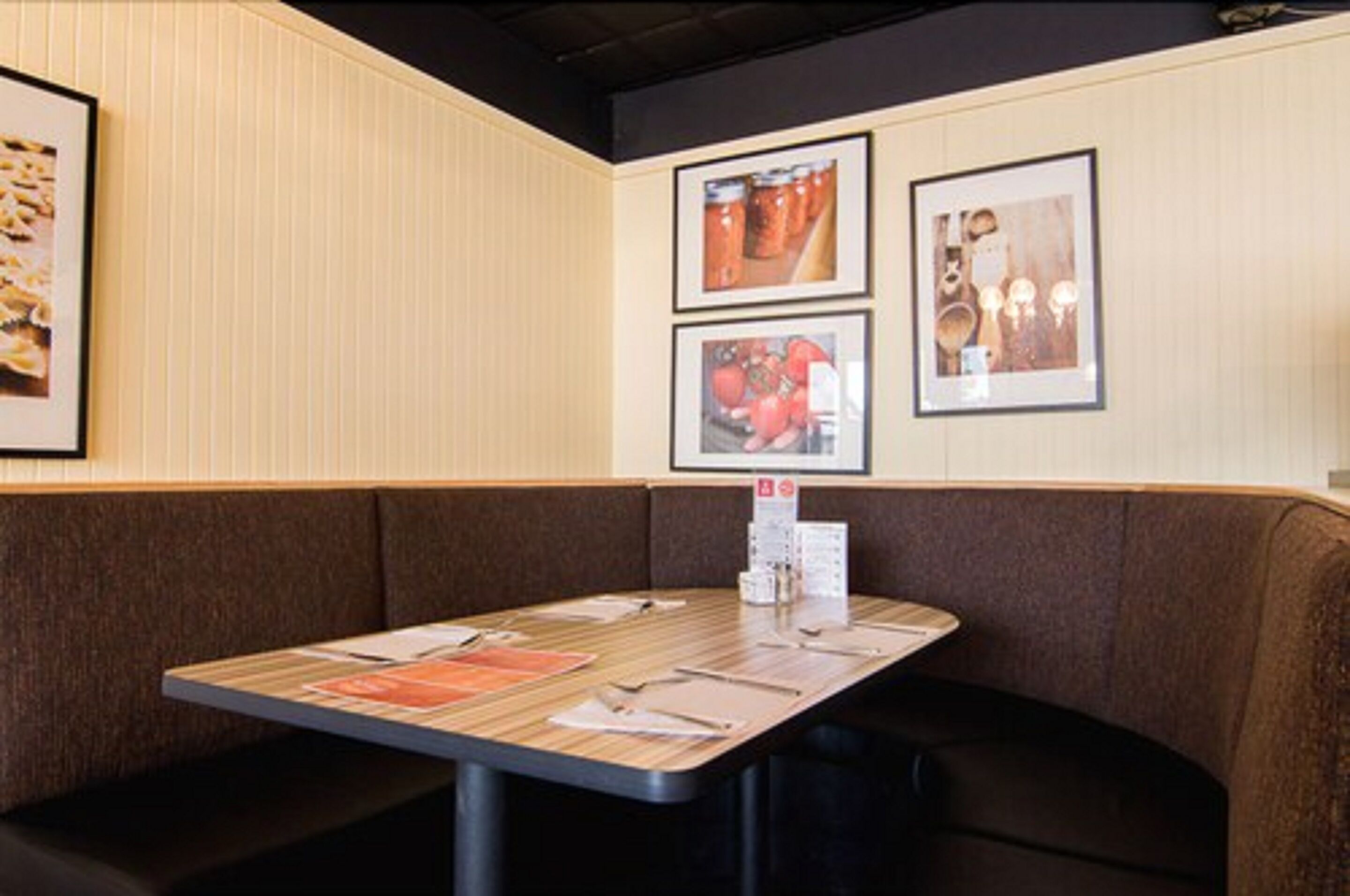 Un restaurante con zona de cabinas, una mesa de madera con menús y cuadros en la pared.