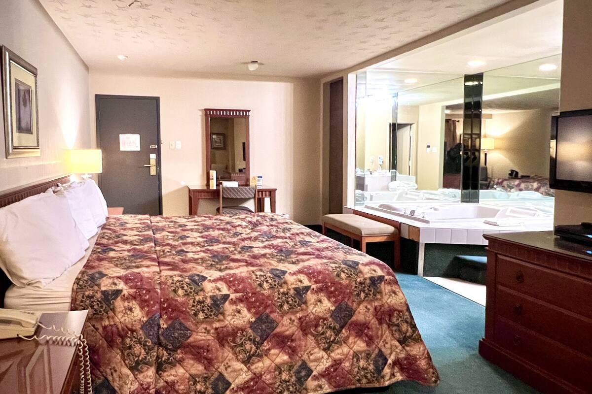 A hotel room with a large bed, a desk, a chair, a dresser, and a television.
