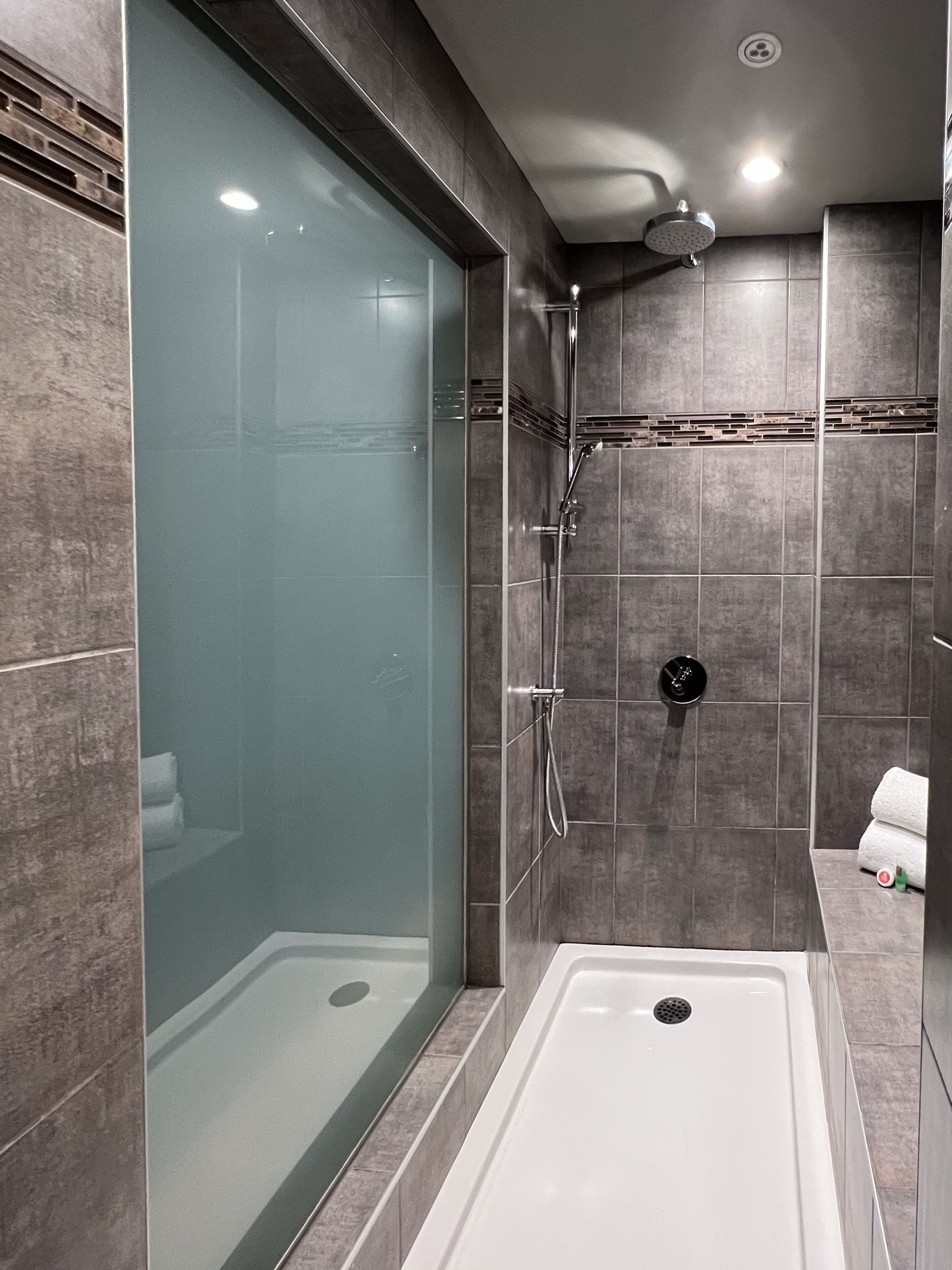 Ein modernes Badezimmer mit einer gläsernen Dusche, einer separaten Badewanne und Fliesenwänden.