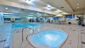 Una piscina interior con un jacuzzi, suelo de baldosas y sillones de descanso.