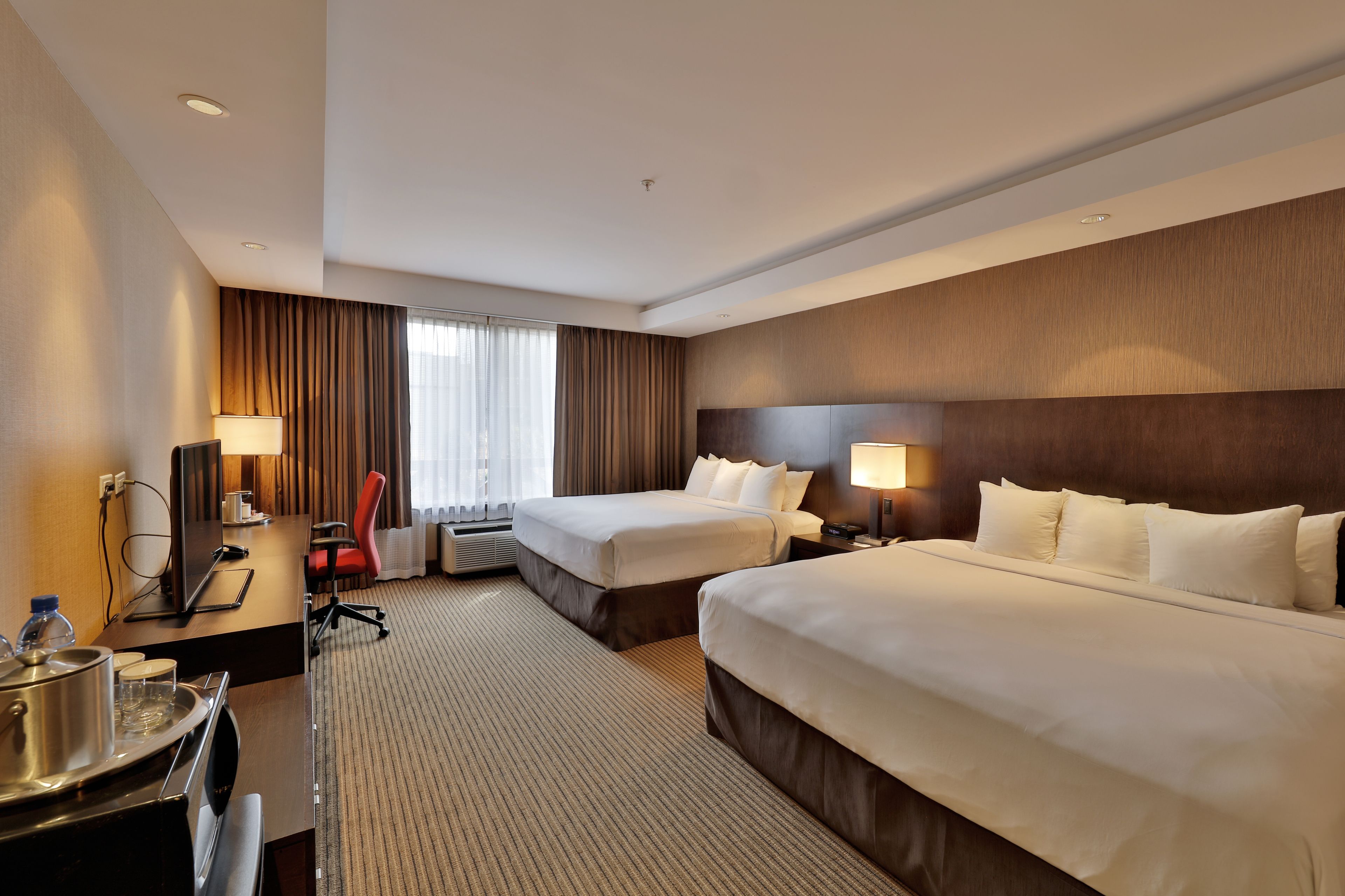 A hotel room with two beds, a desk with a computer, a chair, and a large window with curtains.